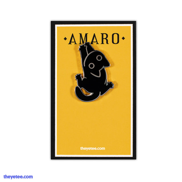 Hard enamel pin of Amaro the black cat hanging on by their front paws affixed to a full-color backing card. - Clingy Amaro